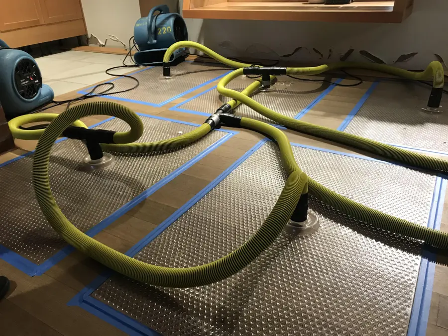 Drying mats and hoses taped over a hardwood floor during structural drying, the setup used for wet wood floors in Encinitas homes