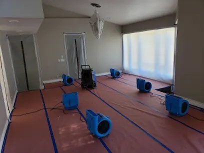 Blue air movers set across a room on floor protection paper during structural drying
