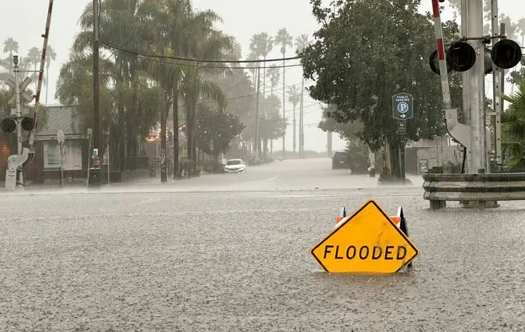 Flooded road beside palm trees and railroad crossing signals in a heavy winter rainstorm, the kind of storm that tests coastal North County drainage