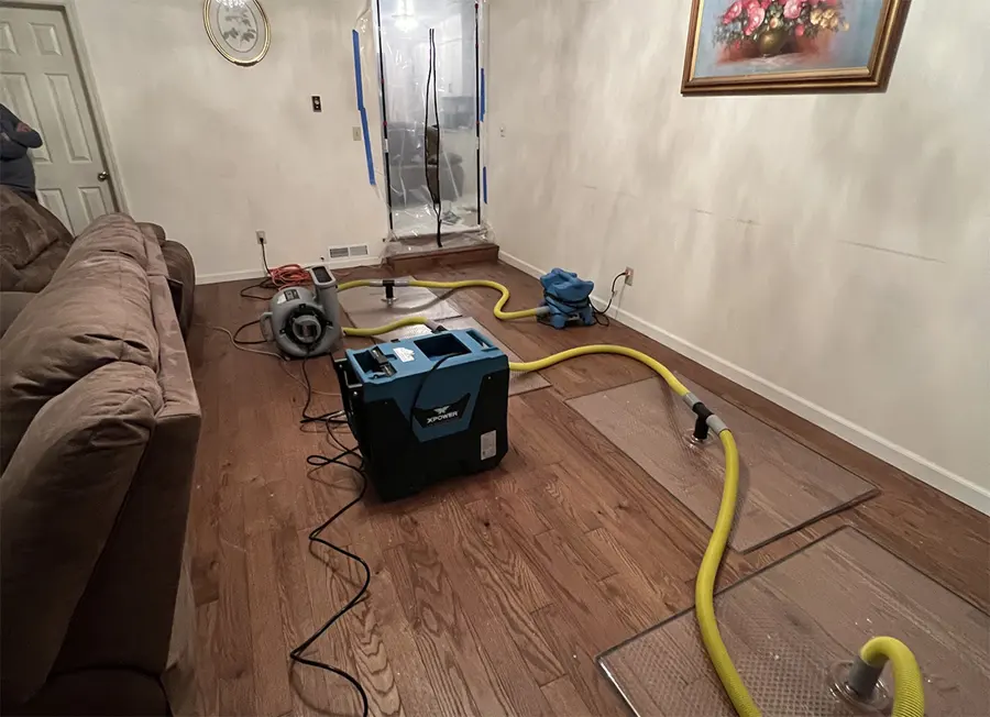 Drying hoses, an air mover and a dehumidifier set up on a wood living room floor, typical of a Carlsbad water damage job