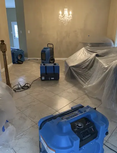 Dining area set up for an Oceanside water damage job, with air movers and a dehumidifier running and the furniture covered in plastic sheeting.
