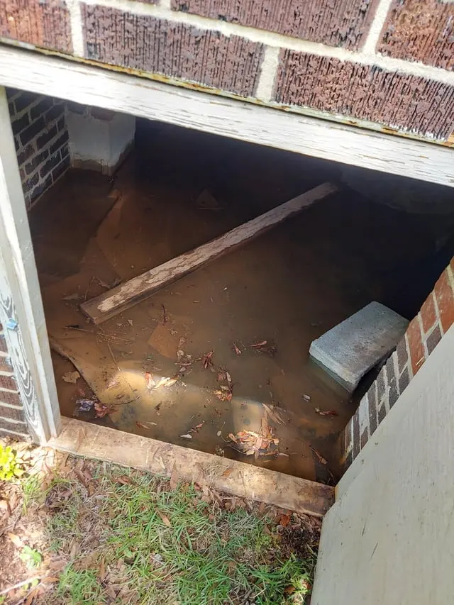 Standing water inside a crawl space seen through the foundation access opening, crawl space water removal in Encinitas