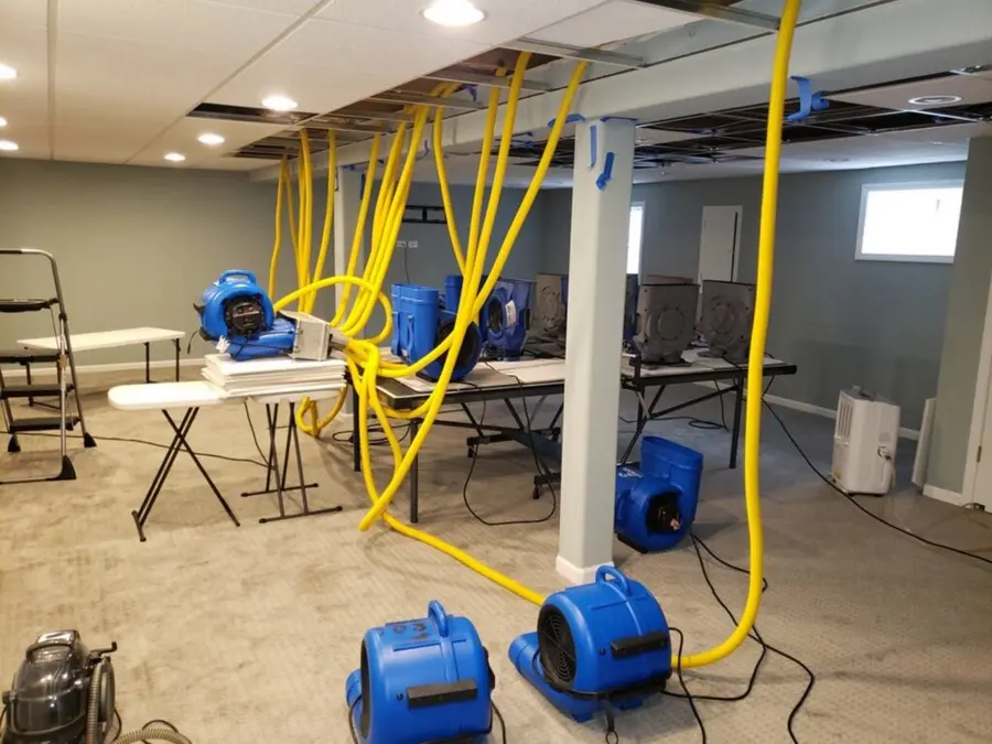 Air movers and ceiling drying hoses running in a lower-level room with the ceiling panels opened, structural drying in Encinitas